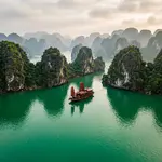 Ha Long Bay limestone karsts rising from emerald water with traditional junk boat